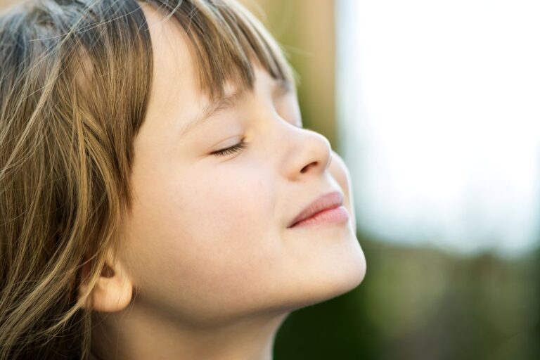 Close-up of a young girl with eyes closed and a peaceful smile, enjoying the breeze.